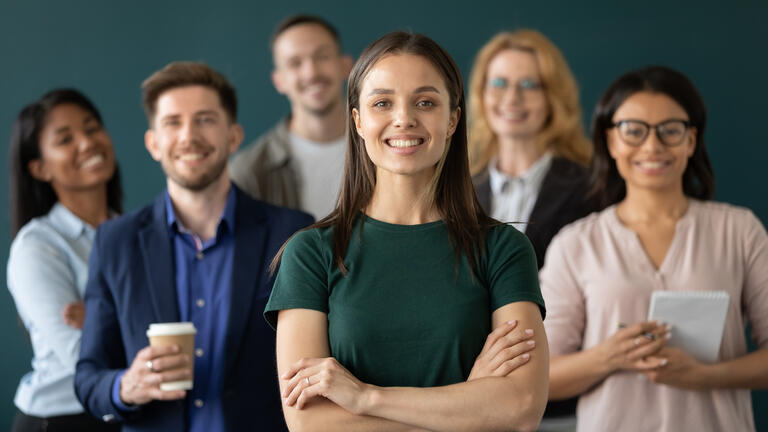 Close up headshot portrait of happy businesswoman hands crossed posture. Different age and ethnicity businesspeople standing behind of female company chief business. Leader of multi-ethnic team concept