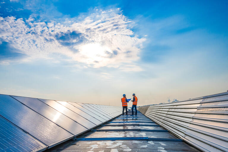 Two technicians in distance discussing between long rows of photovoltaic panels. Alternative energy source, ecology and carbon footprint reduction concept.